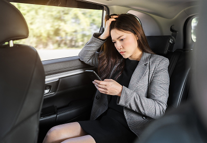 Woman in a gray blazer sitting in a car, looking at her phone with a concerned expression.