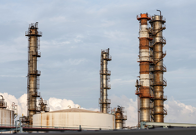 Industrial refinery with three tall metal smokestacks against a cloudy sky, featuring orange and silver colors.