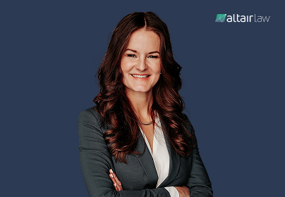 Smiling woman with long brown hair in a gray suit, arms crossed, against a dark blue background with Altair Law logo.